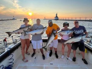 Group of people on a fishing charter on Lake Michigan posing with their fish with the sun setting behind them